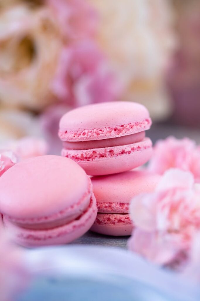 Yummy sweet pink macaroons placed on table against fresh carnation flowers in daylight